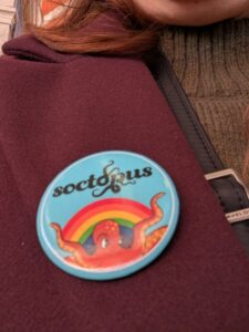 Round blue button saying "soctopus" with a red octopus under a rainbow.